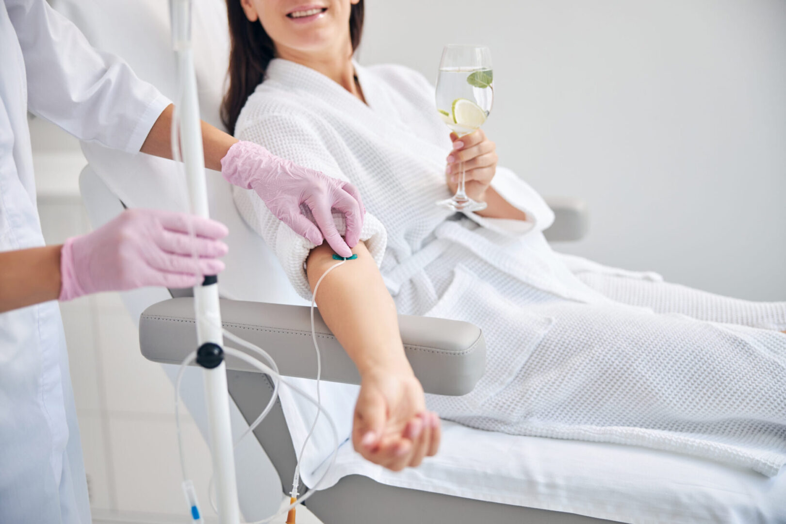 A woman is holding a glass of wine while sitting in a hospital bed.